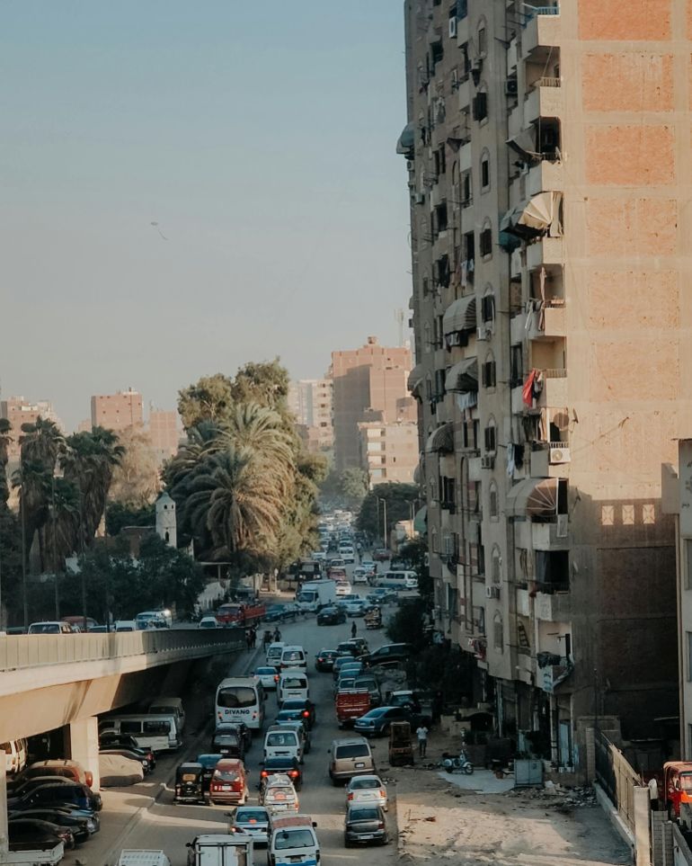 msrr-1780307193 A bustling street in Cairo with traffic and pedestrians against a backdrop of city buildings.