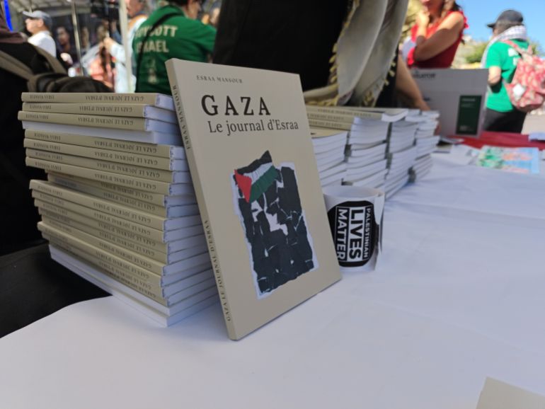 pic-885543-1781373712 PARIS, FRANCE - JUNE 13: A book is seen on the stand as demonstrators wave Palestinian flags during a rally organized by EuroPalestine at the Fontaine des Innocents in Paris, France, on June 13, 2026. Awareness and document distribution stands were set up on site as participants denounced the war in Gaza and reaffirmed their support for the Palestinian people. ( Ümit Dönmez - Anadolu Agency )
