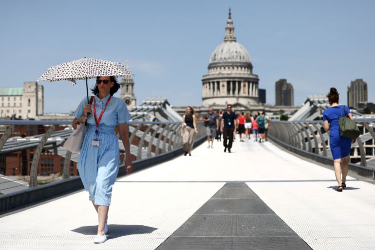 A woman walks with an umbrella along the Millennium Bridge as Britain experiences record temperatures disrupting schools and transport networks in London, Britain, June 23, 2026. REUTERS/Jack Taylor