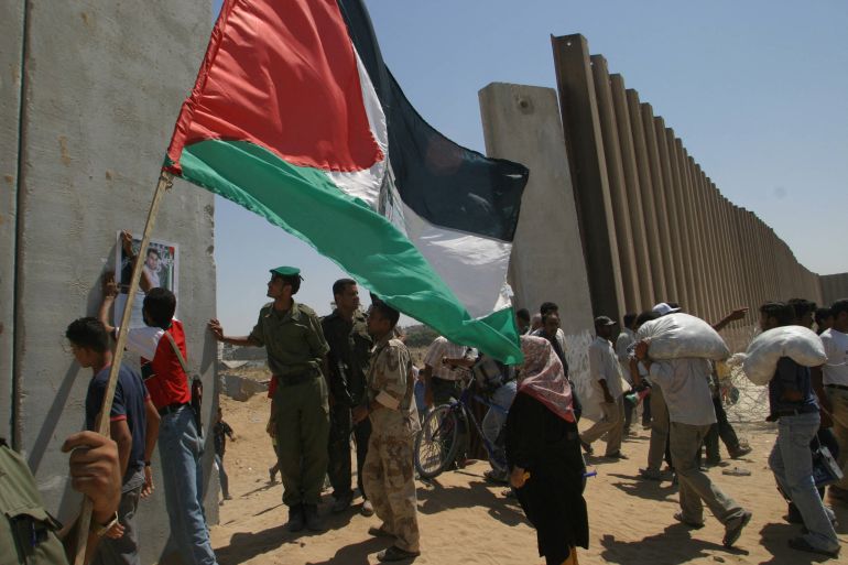 محور صلاح الدين Palestinians, one of them holding a national flag, gather next to the concrete wall, built by Israel, that divides Palestinian Rafah from the Philadelphi Corridor buffer zone on the Gaza-Egypt border, to cross to the other side 13 September 2005. The Rafah border between Egypt and the Gaza Strip, where civilians have been able to cross at will since the departure of Israeli troops, will be closed from midnight (2100 GMT) tonight, a Palestinian official said. AFP PHOTO/MOHAMMED ABED (Photo by Mohammed ABED / AFP)