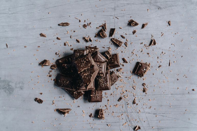 shkwlath-1779695619 Top-down view of broken dark chocolate bars with shavings on a gray background, ideal for food photography.