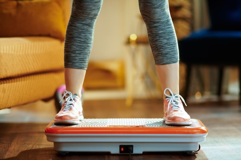 shutterstock_1398930395-1780911020 Closeup on young woman in fitness clothes in the modern house training using vibration power plate.