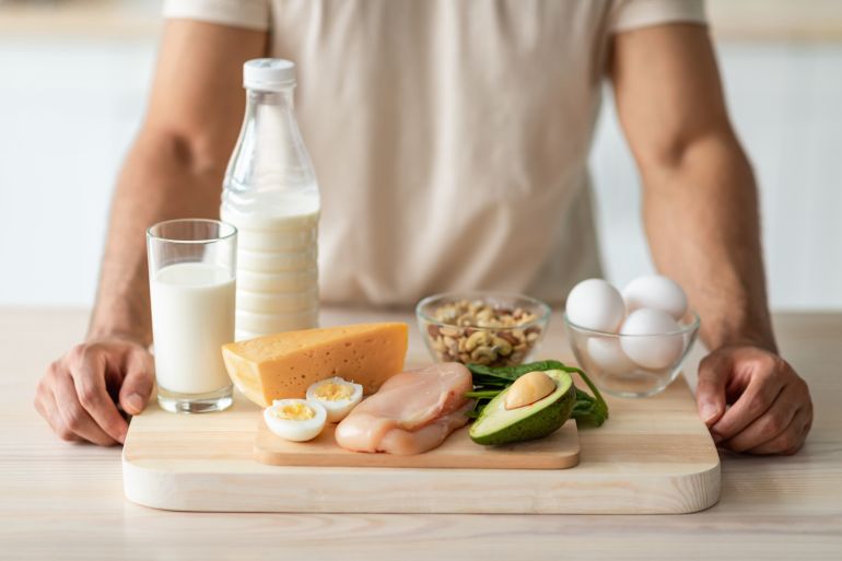 Cropped view of fit young guy standing near wholesome protein products at kitchen, closeup. Unrecognizable sporty man offering healthy nutrition for muscle gain or weight loss