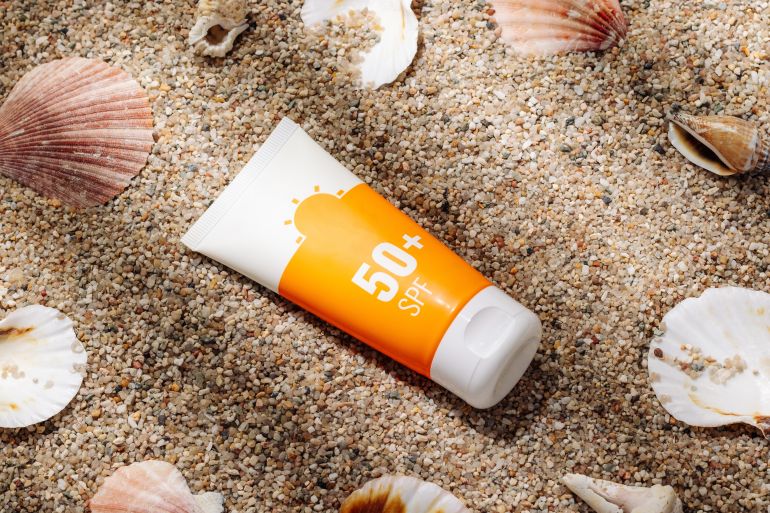 shutterstock_2294194711-1714901217 Orange tube of sunscreen on sandy beach top view