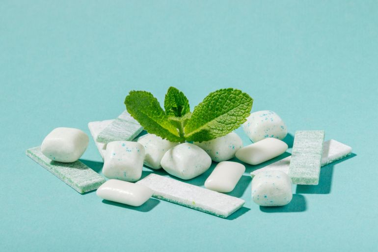 A bunch of mint chewing gum and fresh mint leaves on a blue background