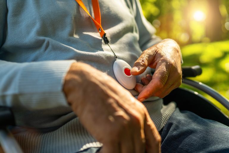Senior man pressing Alarm Button in a wheelchair outside in a park, closeup. Emergency call system concept image.