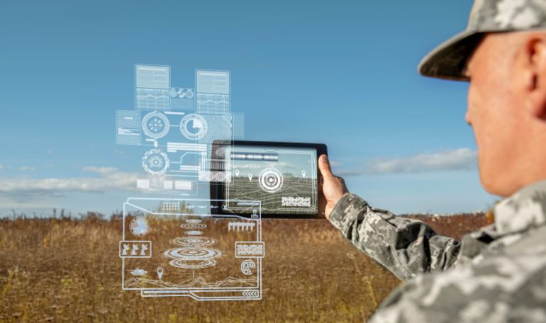 shutterstock_2389206117-1781336704 AI technology in the army. Warfare analytic operator checking coordination of the military team. Military commander with a digital tablet device with artificial intelligence operating troops outdoors.