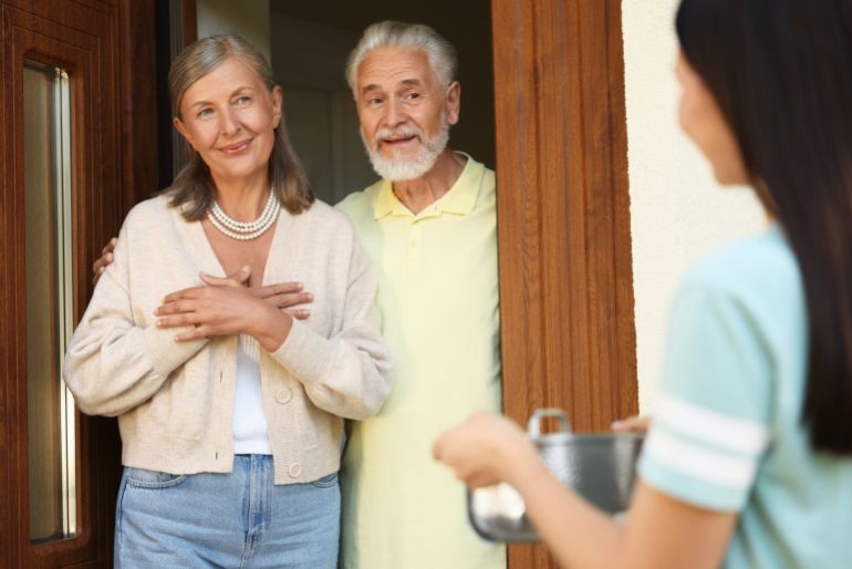 Friendly relationship with neighbours. Young woman with saucepan visiting elderly couple