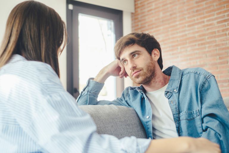 shutterstock_2487054849-1778238786 Serious young couple sitting together on sofa, talking about relationships, spending time together at home, focused wife listening to speaking husband, friends having conversation