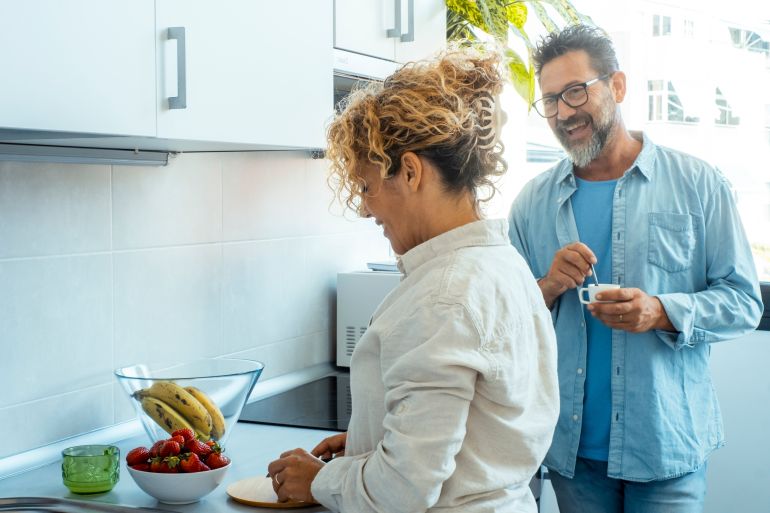 Man and woman in relationship living together talking happy in the kitchen. Adult man and woman preparing breakfast. Morning routine family inside home. One couple enjoying apartment and smiling