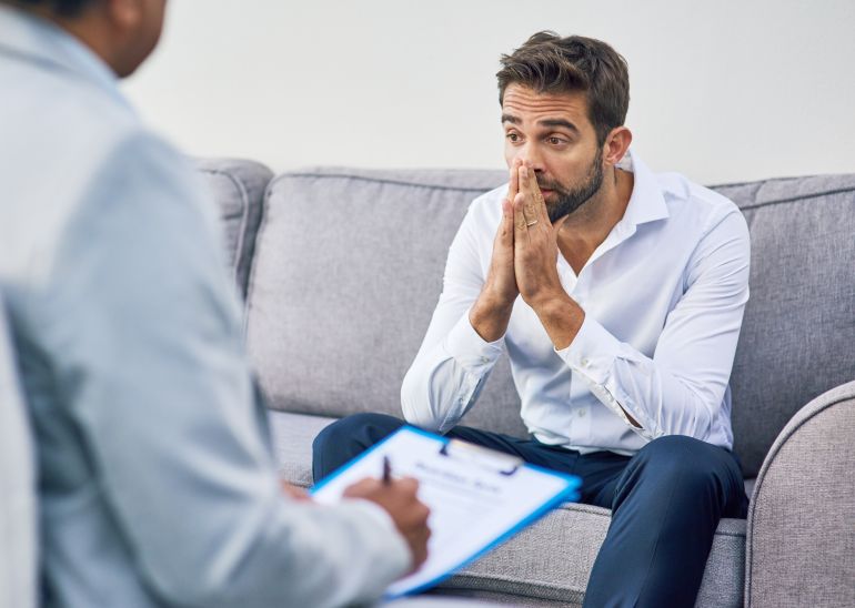 shutterstock_2529332191-1740927362 Man, depression and doctor for therapy in office, psychologist consultation and paper for notes. Patient, therapist and counseling service on sofa for depression, specialist and helping with trauma