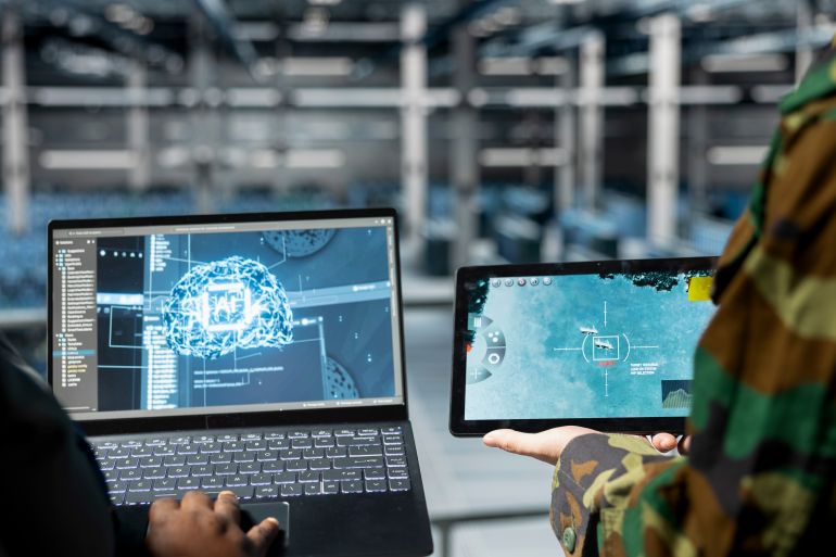 shutterstock_2664762475-1781336720 Close up of military operator and IT expert in army data center using AI on laptop to manage autonomous defense systems. Soldier and programmer using AI for strategic threat detection