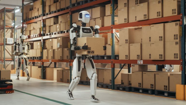 Robotic Worker Walking with a Cardboard Box Inside a Warehouse in a Smart Factory. Humanoid Robot Working in a Logistics Center, Performing Human Tasks with the Help of Artificial Intelligence