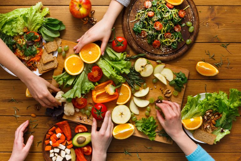 shutterstock_640258210-1715681666 Healthy food dinner table. Women at home together, eating fruits and vegetables, top view, flat lay, crop