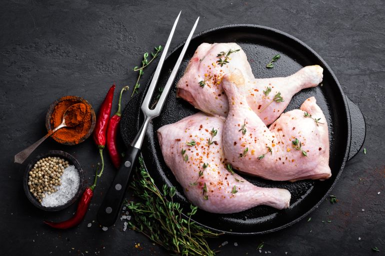 shutterstock_770568403-1744739690 Raw chicken quarters, legs in a pan on a dark background. Top view.