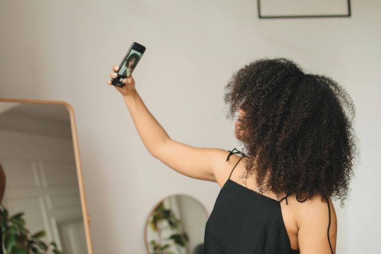slfy-1780055443 A woman with curly hair takes a selfie in front of a mirror at home, capturing a candid moment.