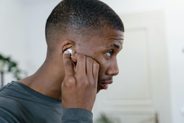 Close-up of a man adjusting his wireless earbuds while indoors, showcasing modern lifestyle.