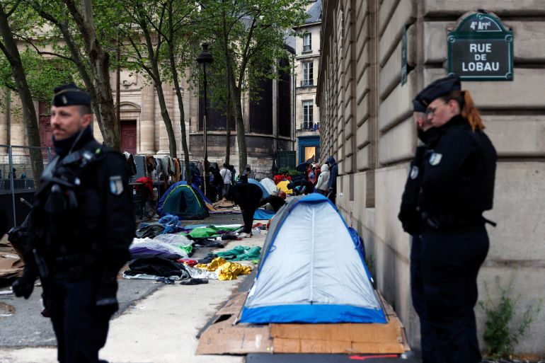 French Gendarmes stand in position as migrants pick up their belongings during the evacuation of their camp on Place Saint-Gervais near Paris City Hall, France, April 30, 2024. REUTERS/Abdul Saboor
