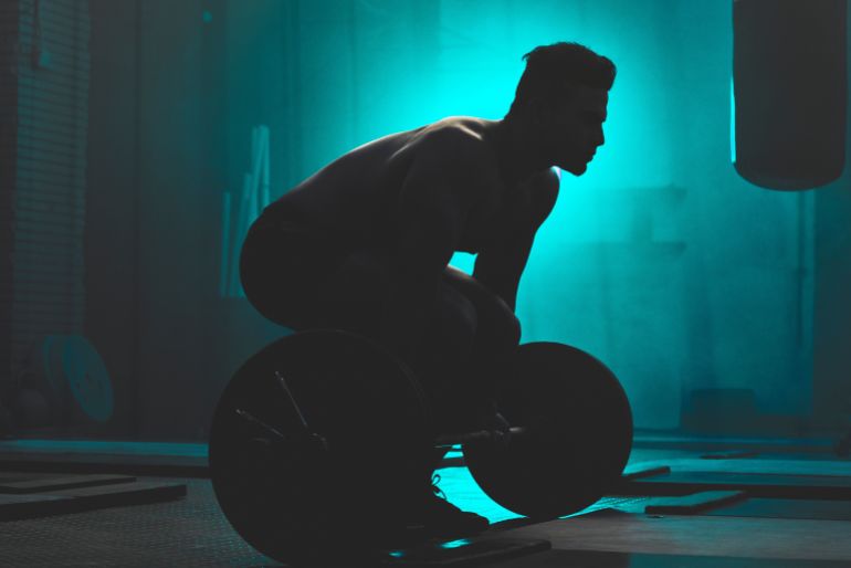 weight-lifting5-1769939009 Silhouette, man and weightlifting with barbell for workout, exercise or training in fitness at gym. Active male person or bodybuilder lifting bar for muscle gain, strength or practice at health club