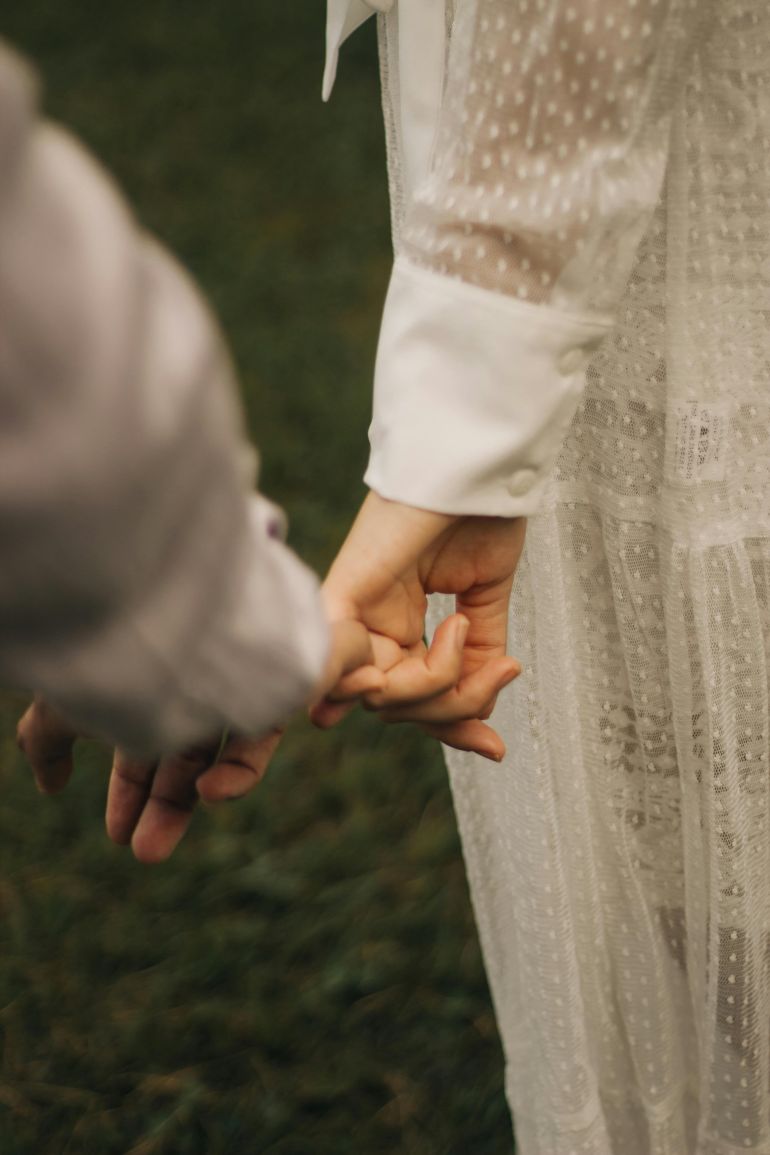 Close-up of a couple holding hands in wedding attire, emphasizing romantic connection.