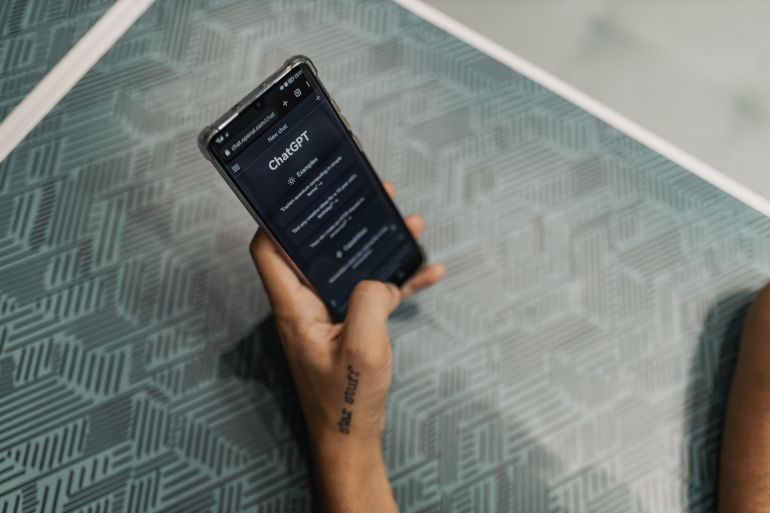 1sfht-acabflam-1782107125 Close-up of a person holding a smartphone displaying the ChatGPT application interface on a patterned table.