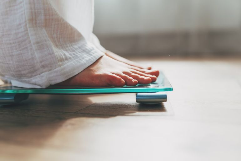 31-1784456610 Female feet standing on electronic scales for weight control on wooden background. The concept of slimming and weight loss