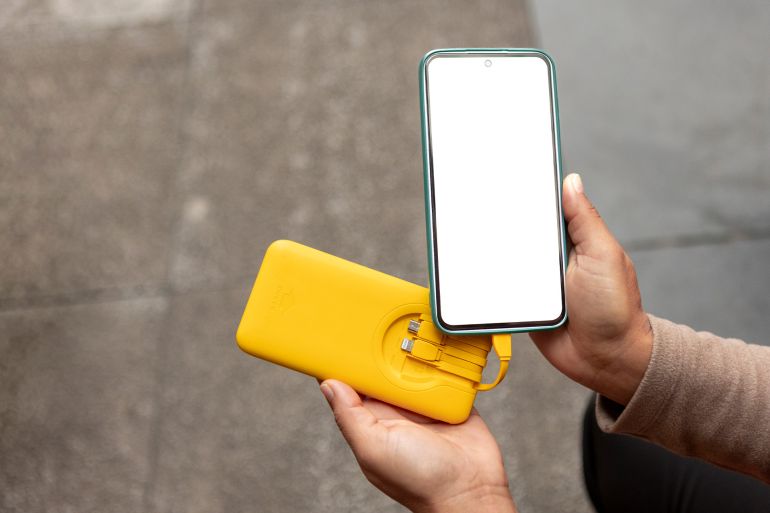 4-1783146247 Mobile phone connected to white external power bank with usb cable on dark background. Portable backup battery charging smartphone screen mockup for travel, technology or emergency energy