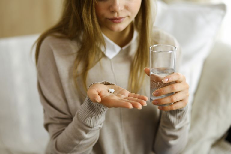 Close-up woman holding pills time to take medications, cure for headache, high blood pressure or cholesterol level remedy pain killer drugs. Stay at home concept during Coronavirus pandemic and self