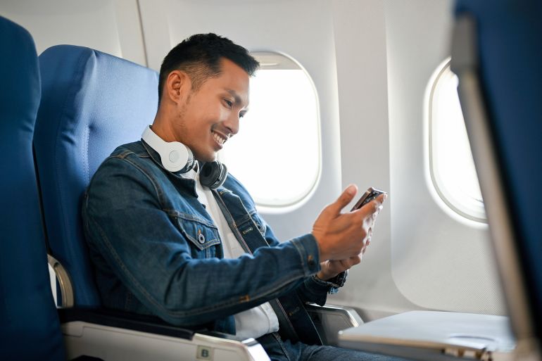 side view, Asian male passenger using his smartphone during the flight. by bongkarn @ادوبي ستوك