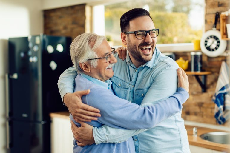 56b-1784633364 Cheerful mature man and his adult son embracing while greeting in the kitchen. المصدر فري بيك