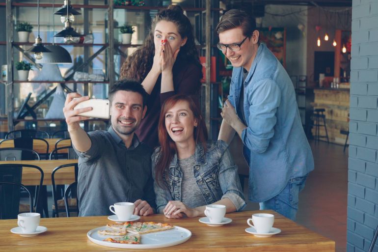 Group of friends taking a selfie in a café while enjoying coffee and pizza, capturing joyful moments