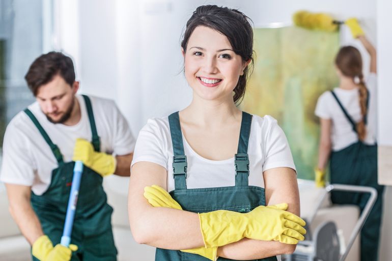Smiling cleaning lady in a green uniform and yellow rubber gloves at work adobe stock
