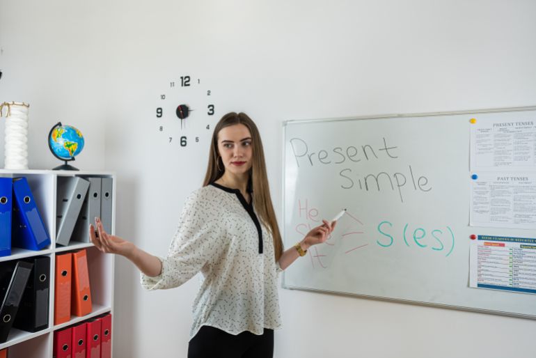 5new-1784023304 Professional female teacher explaining new theme pointing at whiteboard looking and asking students in classroom. adobe stock