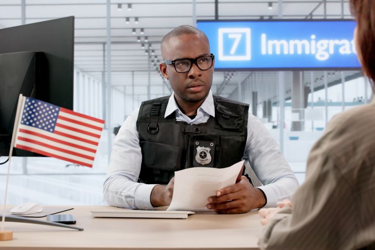 67ty67-1784219147 Woman Waits Anxiously At Airport While Immigration Agent Checks Passport by Andrey Popov @ادوبي ستوك