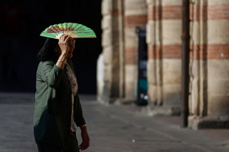 A woman holds a fan over her face to shield herself from the sun during hot weather in Bologna, Italy, June 20, 2026. REUTERS/Vincenzo Livieri