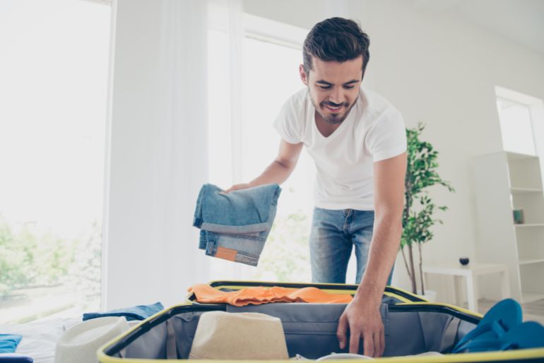 adobestock_215008561-1784648953 Time to fly for the holidays! Happy and joyful young man packing jeans in a suitcase @ادوبي ستوك
