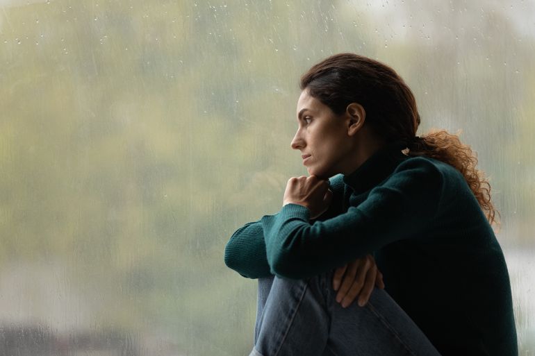 adobestock_449673822-1784563738 Side view frustrated thoughtful woman looking out rainy window in distance alone, lost in thoughts, upset unhappy young female feeling lonely and depressed, thinking about relationship problems المصدر: أدوبي ستوك