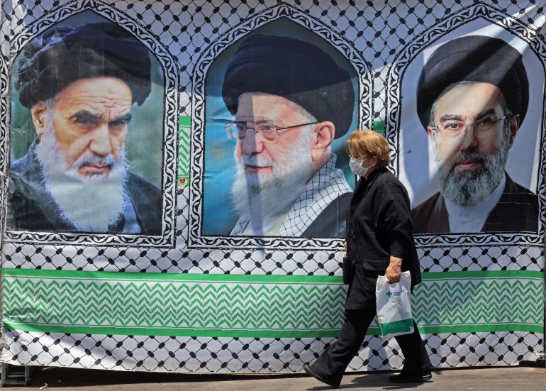 afp_6a2c151458ad-1781273876 A woman walks past a banner bearing the images of the late founder of the Islamic Revolution supreme leader Ayatollah Ruhollah Khomeini (L), the late Iranian supreme leader Ali Khamenei and his son, the current supreme leader Mojtaba Khamenei (R), erected along a street at the Vanak Square in Tehran on June 10, 2026.