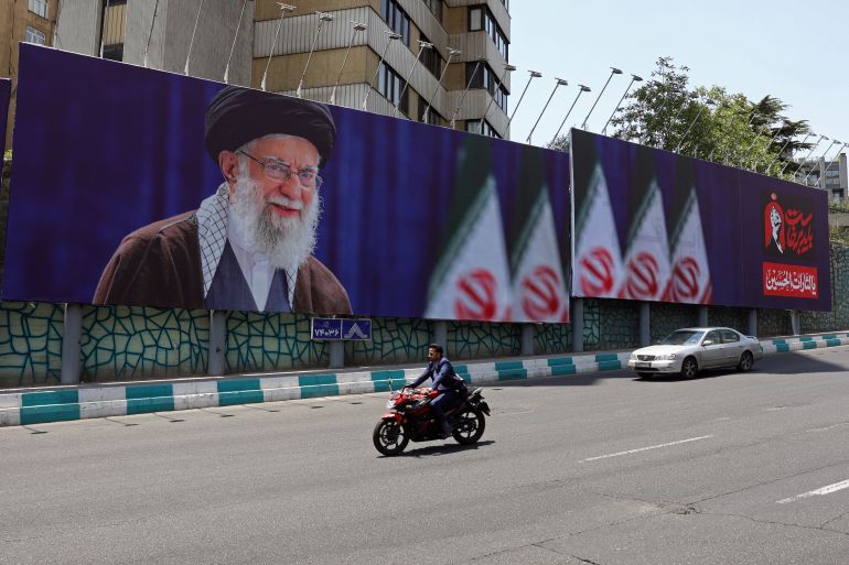 afp_6a4642a299ce-1782989474 Commuters drive past a giant billboard bearing a picture of Iran's late supreme leader Ayatollah Ali Khamenei ahead of his funeral, in Tehran on July 2, 2026.