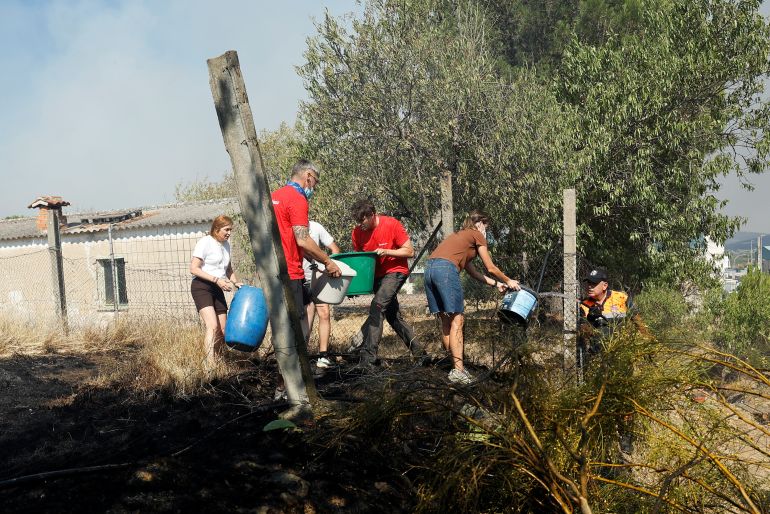 afp_6a663da6b78f-1785085350 Residents carry containers of water to put out the embers as a fire started in an industrial area of San Martin de Valdeiglesias, about 70km west of Madrid, on July 26, 2026.