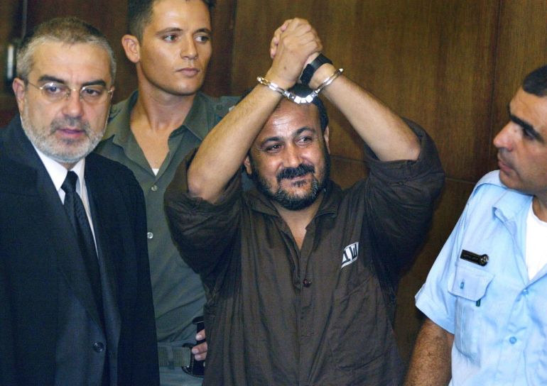ap_690082f36e1df-1761641203 FILE - Marwan Barghouti, center, raises his handcuffed hands in the air on the opening day of his trial in Tel Aviv, Israel, Aug. 14, 2002. (AP Photo/Brennan Linsley, File)