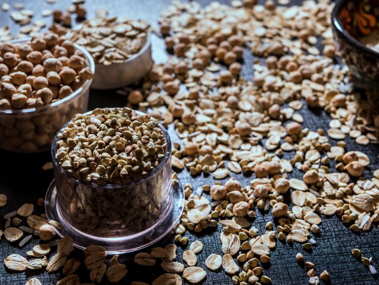 artjacabf-bqwlyat-1782924185 Close-up of diverse grains and legumes in plastic cups on a textured surface, highlighting healthy food options.