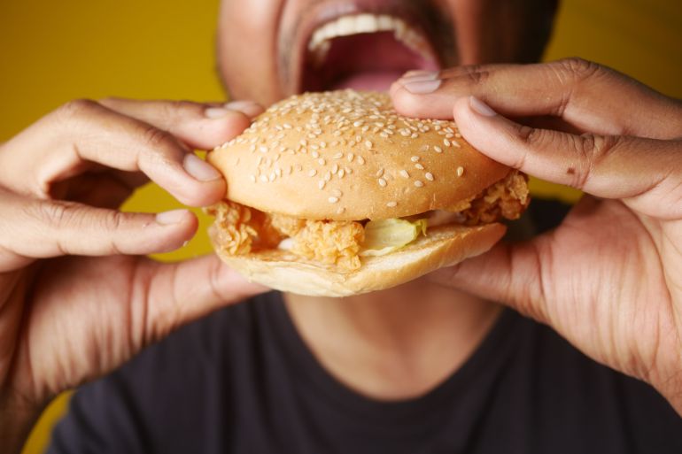 artjacabf-wjbat-srycabft-1782923642 A man enjoying a tasty chicken burger, highlighting fast food cravings and deliciousness.