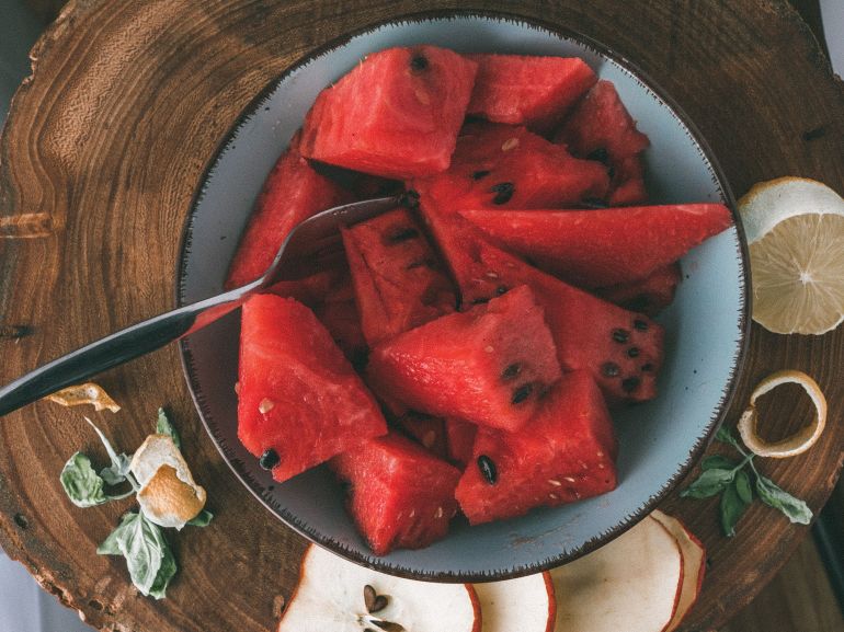 btykh-1782924865 Sliced watermelon in a bowl on a wooden board with citrus and apple accents.