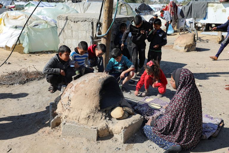 d8b3d98ad8a8d8a7d8ab10-1706257113 A Palestinian woman bakes bread as children sit next to her, while Gaza residents face crisis levels of hunger and soaring malnutrition, in Khan Younis in the southern Gaza Strip January 24, 2024. REUTERS/Arafat Barbakh