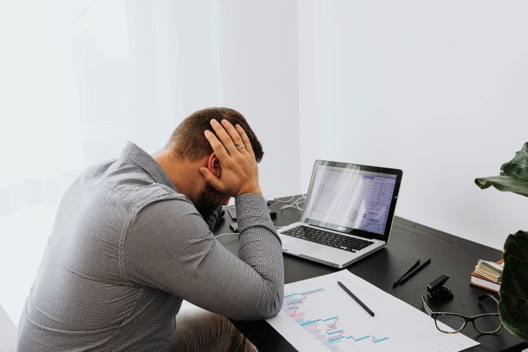 dghwt-alcabfml-1777741858 A man looking stressed at his desk, hands on head, with a laptop and graphs.
