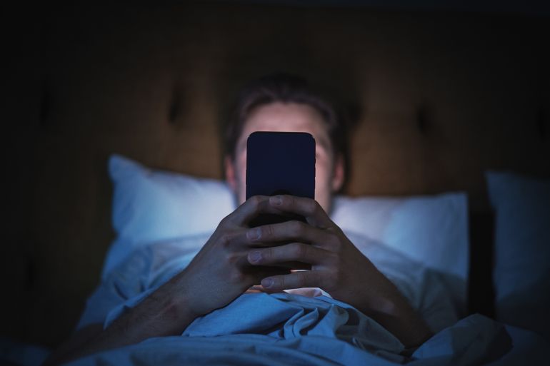 gettyimages-1479322386-1729714668 Anonymous Man Uses Smartphone in Bed at Home at Night. Handsome Guy Browsing Social Media, Reading News, Doing Online Shopping Late at Night. Focus on Hand Holding Mobile Phone Covering Face
