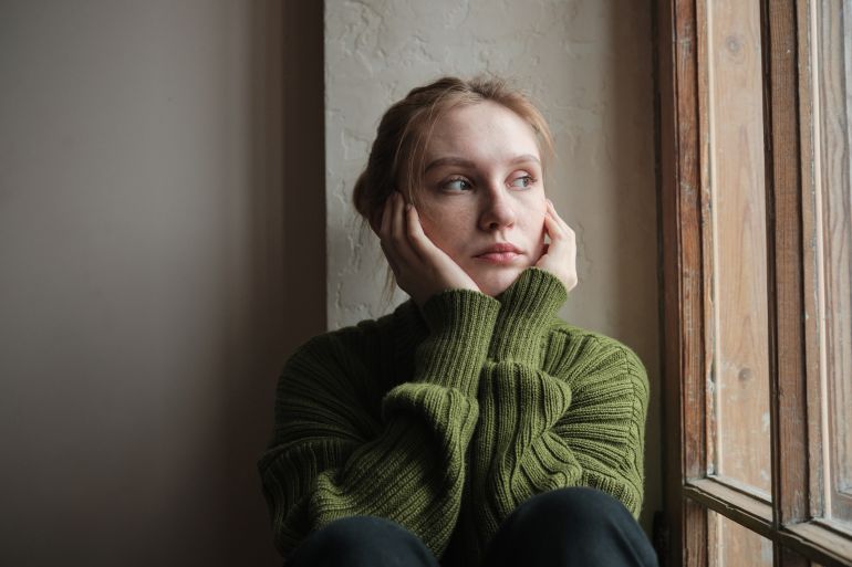 gettyimages-1969517960-1720784887 Sad girl looking out window, depressed upset woman on windowsill at home. Young lonely redhead woman thinking about something, pondering, people and loneliness. Mood swings concept