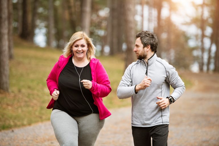 gettyimages-2151435299-1739026855 An overweight woman running in nature with friend. Exercising outdoors for people with obesity, support from friend or fitness coach.