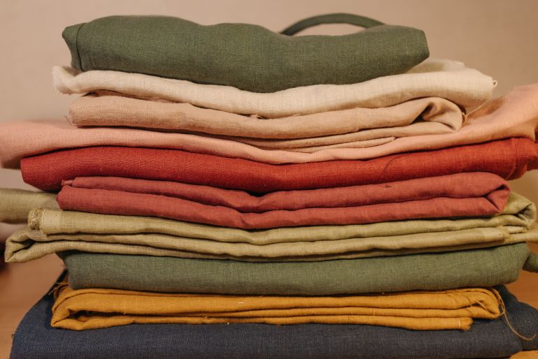 k-6461401-1784379124 Stack of colorful folded fabrics in various textures and colors in a neat arrangement.